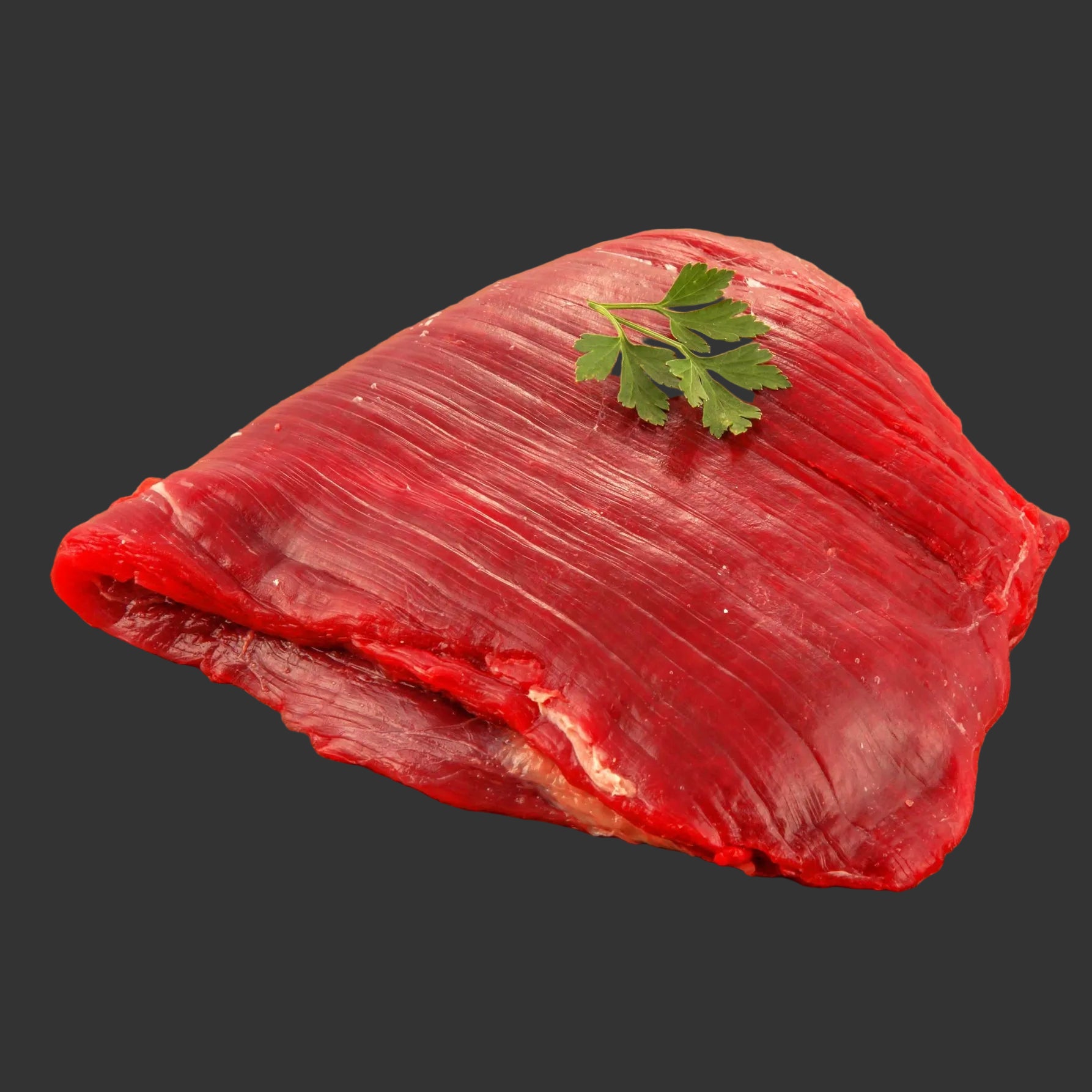Raw beef on a wooden cutting board with a sprig of parsley.
